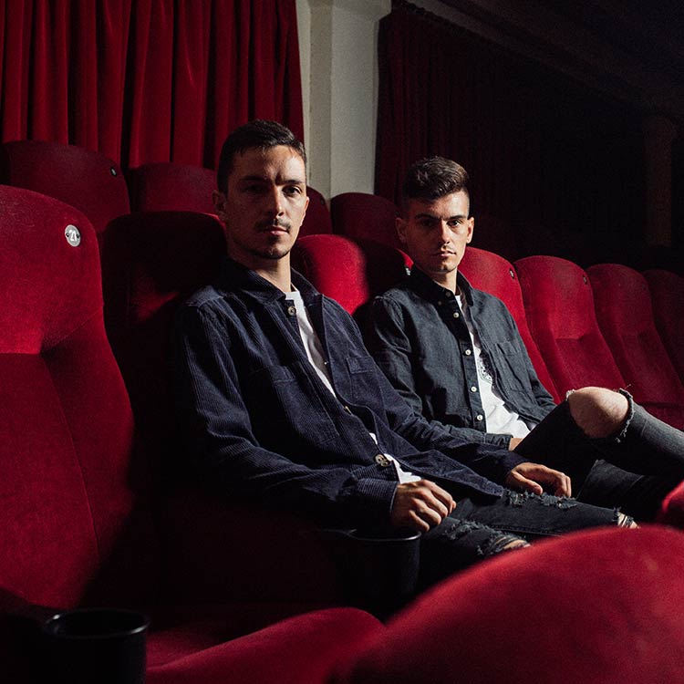 Die Wayford West-Bandmitglieder Max Schmidt und Julian Molinaro sitzen allein nebeneinander in einem Kino mit roten Samtsitzen und schauen bestimmt in die Kamera.